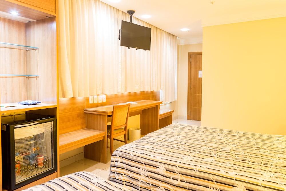 Hotel Atlantico Business Centro Rio de Janeiro Dış mekan fotoğraf The photo shows a hotel room with two beds featuring striped bedding. There is a wooden desk and chair near a window with light-colored curtains. A flat-screen television is mounted on the wall, and there appears to be a small refrigerator or mini-ba